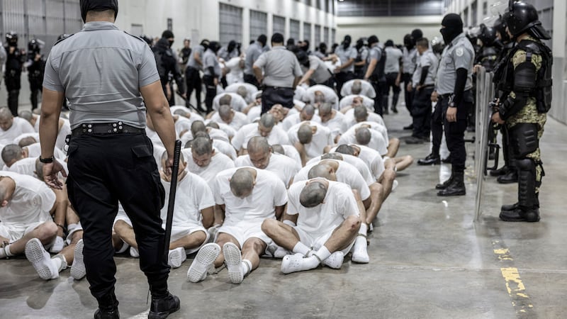 In this photo provided by El Salvador's presidential press office, a prison guard transfers...