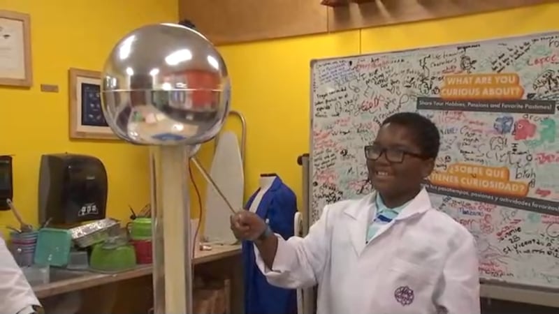 A boy stands in a lab coat playing at a science center.