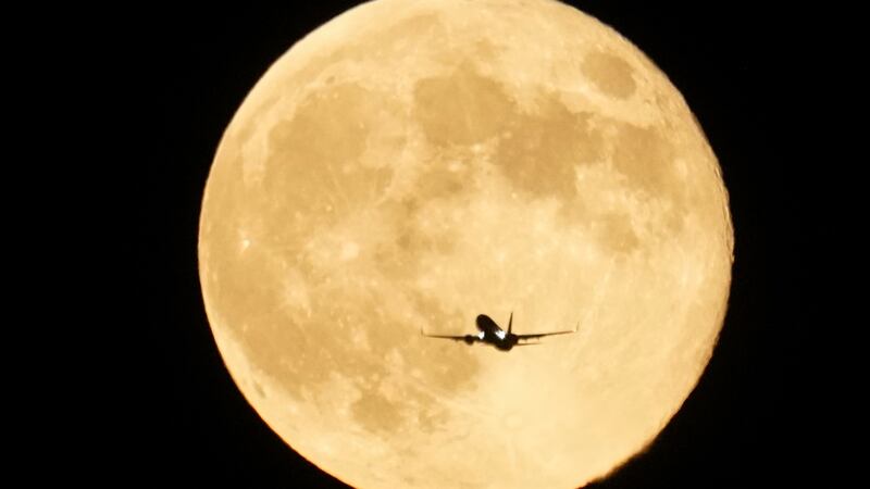 An airplane flies past the moon as it rises over Lake Michigan, Thursday, Oct. 17, 2024, in...