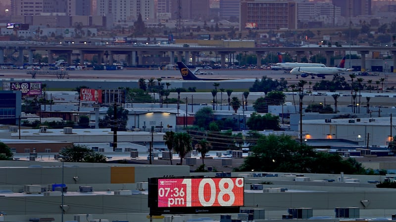 FILE - A sign displays an unofficial temperature as jets taxi at Sky Harbor International...